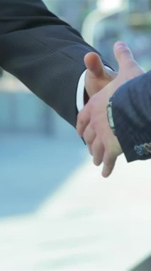 A close-up of two business professionals, one in a sleek dark suit and the other in a stylish patterned blazer, engaging in a firm handshake that symbolizes a powerful partnership. The blurred urban backdrop radiates energy and ambition, capturing