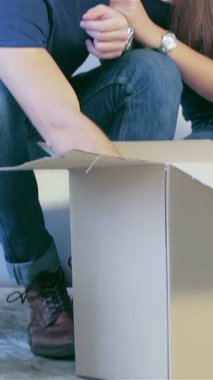 A cheerful couple, radiating joy, sits on a cozy white couch, surrounded by unpacked boxes in their new apartment. Their warm smiles and tender embrace encapsulate the thrill of new beginnings, transforming the empty space into a loving home