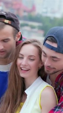 Three lively friends gather under a bright blue sky, sharing laughter and smiles as they assist a girl with her tablet. This vibrant scene radiates the warmth of friendship and the carefree spirit of summer, filled with joy and connection