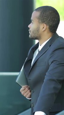 A poised African businessman stands confidently, holding a sleek tablet, as he warmly welcomes new partners against a vibrant urban backdrop. This dynamic scene radiates professionalism and opportunity, capturing the essence of successful business