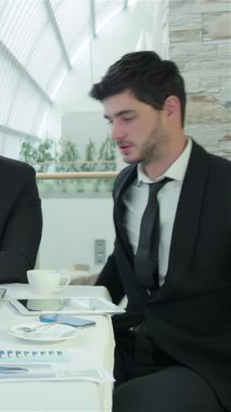 A group of four confident businessmen, dressed in sharp formalwear, are animatedly discussing vital documents in a sleek, modern office filled with natural light. Their enthusiastic gestures and warm smiles create an inviting atmosphere of teamwork