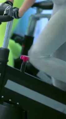 A lively gym scene captures a dynamic group of friends pedaling with fervor on stationary bicycles, their faces radiating determination and focus. The bright neon leggings and colorful workout gear amplify the energetic atmosphere, while their