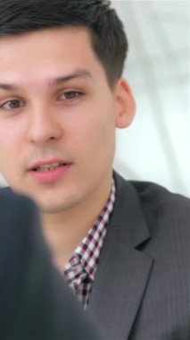 In a sleek, modern office, a young, attractive man in a tailored suit passionately discusses a business project with a colleague, embodying a vibrant atmosphere of collaboration. Their focused expressions and the bright, airy workspace around them