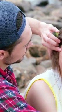 A young man lovingly brushes his friends hair back, their laughter echoing by the shimmering waters edge, surrounded by smooth, sun-kissed stones. This heartwarming scene encapsulates the joy of friendship and the carefree spirit of summer