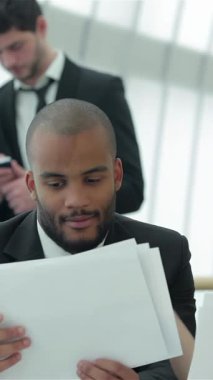 Gösterişli, güneşli bir ofiste, kendine güvenen kızıl saçlı ve gözlüklü bir kadın, her ikisi de önemli belgeleri dikkatle inceleyen iyi giyimli bir adamla tutkuyla stratejilerini tartışıyor. Bu arada, iki profesyonel daha, odaklanmış bir adam ve bir kadın.