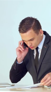 Gösterişli, siyah bir takım elbise giymiş kararlı genç bir işadamı, önemli bir telefon görüşmesi yaparken, cilalanmış masasındaki önemli belgeleri dikkatle incelerken, kendinden emin bir şekilde gülümsüyor. Parlak, modern ofis dekoru, şık bir dizüstü bilgisayar ve