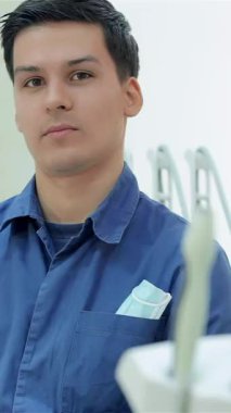 Kendine güvenen mavi üniformalı bir dişçi, parlak bir gülümsemeyle, parlak bir gülümsemeyle, gösterişli, modern bir diş muayenehanesinde pozitiflik yayıyor. Parlak diş aletleri ve el değmemiş çevre davetkar bir ortam yaratıyor.