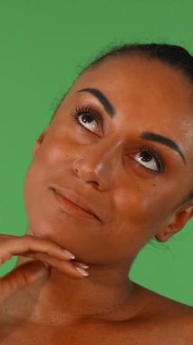 Bu büyüleyici stüdyo portresi, kendinden emin bir Afrikalı kadının boynu hafifçe okşayışını, parlak yeşil renkli arkaplanı aydınlatan gülüşünü gösteriyor. Parlak cildi ve zarif tavırları canlılık ve kendini sevme duygusunu çağrıştırıyor.