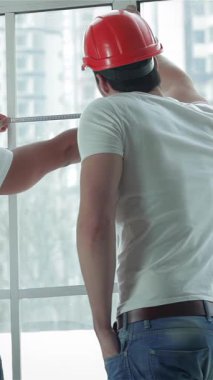 Parlak, havadar bir dairede, kendini adamış iki işçi pencereleri dikkatlice ölçüyorlar ve gerekli onarımlara hazırlanıyorlar. Odaklanmış ifadeleri ve işbirlikçi ruhları, yakınlarda bir merdiven ile parıldıyor, güzel bir iç mekan vaat ediyor.