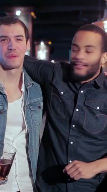 Canlı bir bar ortamında, biri şık sakallı, diğeri de klasik kot yelekli iki eski arkadaş, içkilerimizi içerek kahkahalarımızı paylaşıyoruz. Canlı atmosfer kadeh tokuşturma sesleri ve neşeli şakalarla doludur.