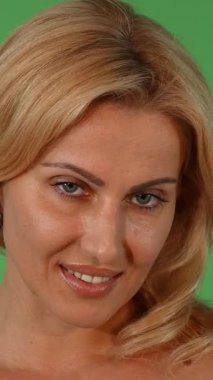 Bu çarpıcı stüdyo portresi çarpıcı bir sarışın kadın sergiliyor, kendine güveni ve cazibesi yayılıyor canlı yeşil renkli bir arka planda baştan çıkarıcı bir şekilde gülümsüyor. Parlak cildi ve zarif duruşu kadınlığın özünü yansıtıyor.