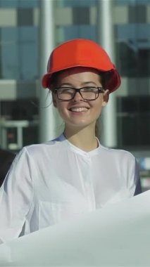 Parlak turuncu bir mimar ve şık gözlükleri olan kendine güvenen bir kadın mimar, hareketli bir inşaat alanının planlarını gözden geçirirken coşkuyla ışıldıyor. Enerjik enerjisi ve profesyonelliği yenilik ruhunu somutlaştırıyor.