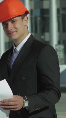 Üç kendine güvenen mimar, parlak turuncu miğferler takmış, şevkle planlarını gözden geçiriyorlar, takım çalışması ve profesyonelliği somutlaştırıyorlar. Bu yenilikçi yapının geleceğini öngördüklerinde dinamik işbirlikleri enerji yayıyor.