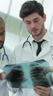 Pürüzsüz, güneşli bir hastane ortamında üç özel doktor ve bir kadın sağlıklı akciğerlerin röntgenini inceliyor. Odaklanmış ifadeleri ve beyaz önlükleri hasta bakımına olan bağlılıklarını yansıtıyor.