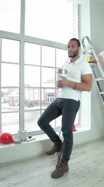 İki hevesli genç müteahhit, biri merdiven üzerinde dengede dururken diğeri de büyük bir pencerenin önünde gururla boya kutularını tutarak başparmak kaldırarak geniş, güneşli bir daireye güven yayıyorlar. Işıl ışıl gülümsemeleri ve enerjik enerjileri