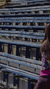 Kararlı genç bir kız, hareketli bir stadyumda heyecan verici bir yarışa hazırlanırken bacaklarına ve ayaklarına odaklanıyor. Renkli koltuklar hareketli bir zemin oluşturuyor, atletik kıyafetlerini büyütüyor ve...