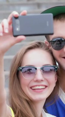 Three vibrant friends, glowing with joy, gather on sun-drenched steps to snap a lively selfie, their radiant smiles lighting up the scene. This delightful moment encapsulates the spirit of friendship and carefree summer days, highlighted by their