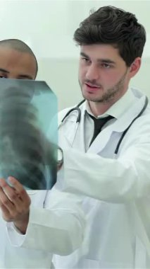 In a state-of-the-art hospital, three confident doctors, including a woman with glasses and two men in crisp white coats, intently analyze an x-ray of healthy lungs. Their focused expressions and collaborative spirit underscore the vital role of