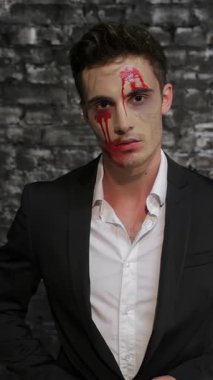A striking male vampire in a sleek black suit wipes blood from his mouth, standing against a textured black brick wall. This chilling image captures the essence of Halloween, blending elegance with horror, as the vampires intense gaze and smeared