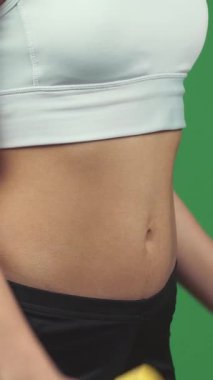 This electrifying close-up features a determined woman with sculpted abs, confidently lifting vibrant yellow dumbbells against a lively green chromakey backdrop. Her intense focus and powerful grip radiate strength and motivation, embodying the