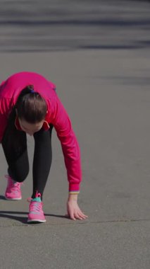A determined young girl crouches at the vibrant starting line of a stadium track, ready to unleash her speed. Clad in bright pink athletic gear, she embodies the spirit of competition, with the smooth gray surface beneath her enhancing the thrill of