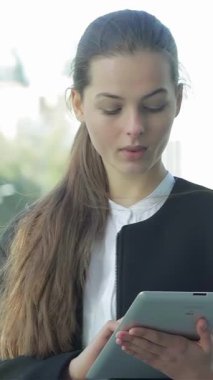 A poised businesswoman stands outdoors, deeply engaged with partners on her tablet, radiating confidence and professionalism. The vibrant urban backdrop amplifies the atmosphere of success and collaboration, highlighting her as a pivotal figure in