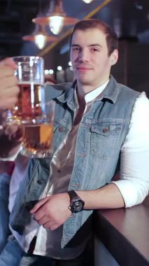 In a vibrant bar scene, two jubilant friends raise their frosty beer mugs in a spirited toast, radiating joy and camaraderie. The lively atmosphere buzzes with excitement as they cheer for their favorite soccer team, encapsulating the essence of