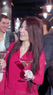 A lively bar scene captures a group of young friends, with girls elegantly holding martinis and guys savoring chilled beers, celebrating in high spirits. The air is filled with laughter and cheers as they toast to their favorite football team