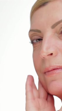 A graceful middle-aged woman gently caresses her cheek, emphasizing her luminous skin against a pristine white backdrop. This stunning portrait radiates beauty and confidence, embodying the essence of self-care and timeless elegance