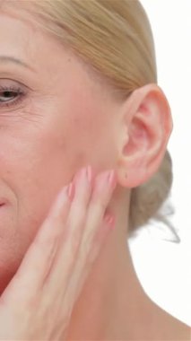 A poised middle-aged woman gently caresses her jawline, showcasing her luminous skin against a pristine white backdrop. This striking portrait radiates beauty and confidence, embodying the essence of self-care and timeless sophistication
