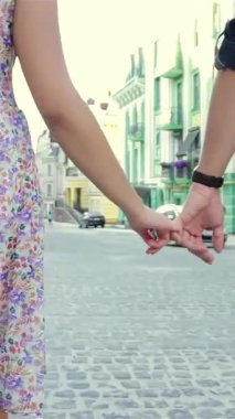 A joyful couple strolls hand in hand along a picturesque cobblestone street, exuding love and happiness. The young woman in a vibrant floral dress and the man in casual attire create a lively scene, embodying the spirit of adventure and romance in