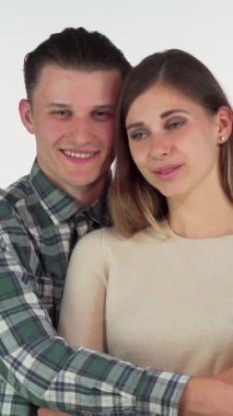 A cheerful young man in a stylish plaid shirt wraps his arms around his lovely girlfriend, exuding warmth and affection in a bright studio setting. Their radiant smiles and sparkling eyes reflect a deep emotional connection, celebrating the joy of