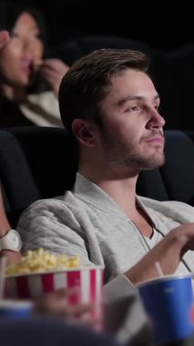 A captivated audience, filled with young adults, shares laughter and emotions in a cozy theater, immersed in the cinematic experience. With vibrant popcorn buckets and refreshing drinks, this lively scene radiates joy and camaraderie, showcasing the