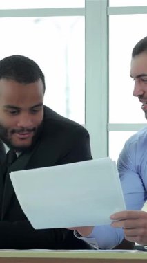 In a bright, contemporary office, two confident businessmen engage in a dynamic discussion, intently reviewing important documents. Their sharp formal attire and focused expressions radiate professionalism, showcasing the essence of teamwork and