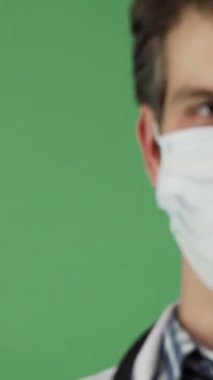 A cropped portrait of a joyful male doctor, wearing a protective medical mask, showcases his confident demeanor against a lively green chromakey background. His bright smile and professional attire radiate trust and dedication, inviting a sense of