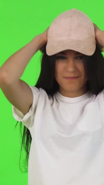 Şık, genç bir esmer, pembe beyzbol şapkasını, canlı yeşil bir arka plana karşı neşeyle ayarlıyor. Bu modaya uyan genç, günlük beyaz tişörtler giymiş, gençlik enerjisini ve modern yeteneğini somutlaştırıyor, izleyicileri kendi coşkusuna davet ediyor.