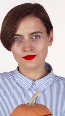 Neşeli, kırmızı dudaklı bir kadın şakacı bir şekilde yüzünü oyulmuş bir balkabağı fenerinin arkasına gizliyor, neşeli bir neşe saçıyor. Bu büyüleyici sahne, Cadılar Bayramı ruhunu yansıtıyor. Gelenek ve eğlenceyi, ılık sonbaharın ortasında harmanlıyor.