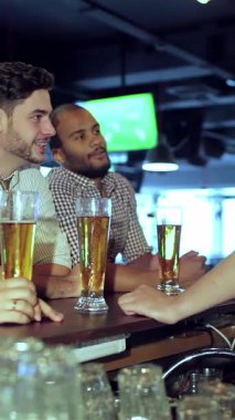 Canlı bir sahne, ellerinde buzlu birayla en sevdikleri futbol takımına tezahürat ederken kahkahalarını ve heyecanlarını paylaşan dört genç adamı büyük ekranda yakalıyor. Hayat dolu bar atmosferi, yoldaşlık ve neşe dolu seslerle dolu.