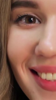 Bu büyüleyici yakın plan, göz kamaştırıcı bir gülüşü olan, beyaz bir arka planda parıldayan, neşeli, genç, beyaz bir kızı gösteriyor. Işıl ışıl gözleri ve canlı kırmızı dudakları pozitiflik ve sıcaklık saçıyor. Seyircileri tadını çıkarmaya çağırıyor.