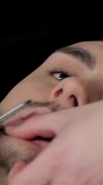 Şık bir genç adam lüks bir berber koltuğunda uzanmış yetenekli bir berberin eski moda tıraşının tadını çıkarıyor. Ambiyans, zengin ahşap aksanları ve tıraş köpüğünün aromatik kokusuyla ahenkli bir karışım yaratıyor.