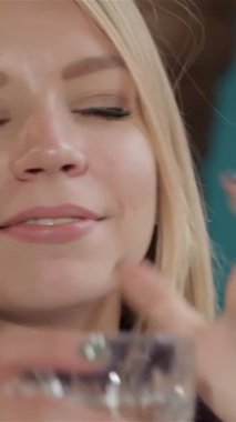 Çekici beyaz bir kadın dalgalı sarı saçlarıyla düşünceli bir şekilde yan tarafa bakıyor, ferahlatıcı bir bardak içeceği sallıyor. Canlı renkler ve yumuşak ışıklandırmayla süslenmiş samimi kafeterya havası rahatlatıcı tavrını geliştirir.