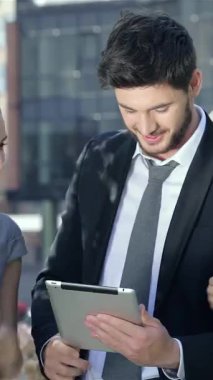 Canlı bir şehir ofis ortamında, şık takım elbiseli üç dinamik iş adamı ve iki şık kadın başarılarını bir tabletle uğraşırken neşeli bir gülümsemeyle kutluyorlar. Şık kıyafetleri ve ışıl ışıl ifadeleri...