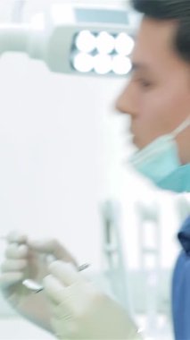 Kendini işine adamış mavi üniformalı ve koruyucu maskeli genç bir dişçi şık ve modern bir klinikte özel diş aletleri kullanarak hastaların dişlerini dikkatle inceler. Bu samimi sahne, profesyonel dişçiliğin hayati önemini vurgular.
