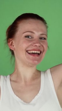 Canlı bir stüdyo çekiminde parlak kızıl saçlı genç bir kadın ışıl ışıl gülümsüyor ve parlak yeşil renkli bir arka plana başparmak sallıyor. Bulaşıcı neşesi ve coşkusu bir kutlama ruhunu somutlaştırıyor.