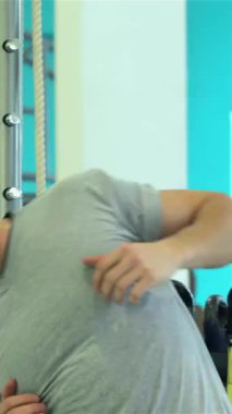 Güçlü fiziği olan kararlı bir genç adam renkli ekipmanlarla çevrili canlı bir spor salonunda enerjik bir omuz kemeri takıyor. Odaklanmış ifadesi ve uygun atletik giysisi kendini spora adamış, vücut bulmuş.