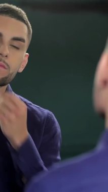 Taze saç kesimi olan şık bir genç adam parlak bir berber aynasında yansımasına hayran kalır, büyüleyici ve stil sahibi. Enerjik atmosfer, kişisel bakım ve modern zarafetin moda ortamında buluştuğu tımarcılığın sanatsallığını vurguluyor.