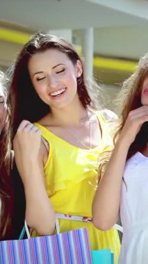 Renkli alışveriş torbaları taşıyan üç modaya uygun kadın şık bir alışveriş merkezinin dışında selfie çekerken neşe saçıyorlar. Işıl ışıl gülüşleri ve kaygısız kahkahaları, güneşli bir günde arkadaşlığın ruhunu ve perakende terapisinin heyecanını temsil eder.