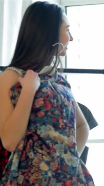 Parlak, havadar bir odada, şık bir kız arkadaş yansımasına ışıldıyor, canlı çiçekli kıyafetini sergiliyor arkadaşları da coşku ve hayranlıkla tezahürat yapıyor. Bu canlı sahne moda keşiflerinin ve derin bağların neşesini yakalıyor.