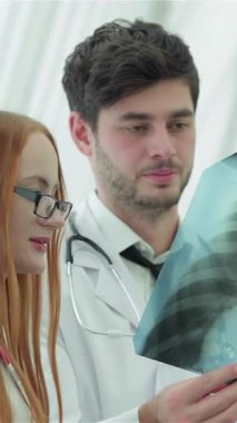 Parlak, modern bir klinikte, her ikisi de beyaz önlük giymiş bir kadın ve erkek doktor, sigara içmenin kritik sağlık etkilerini tartışmak için akciğer röntgenini dikkatle analiz ediyor. Sözleşmeli ifadeleri ve mesleki tavırları hayati önem taşıyor.