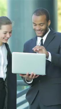 Bir çift gülümseyen iş adamı, şık resmi kıyafetler giymiş bir erkek ve bir kadın, bir dizüstü bilgisayarla hevesle meşgul oluyorlar, işbirliği ve yenilikleri somutlaştırıyorlar. Bu canlı sahne, modern bir şehir zeminine karşı, pozitif ışık saçıyor.